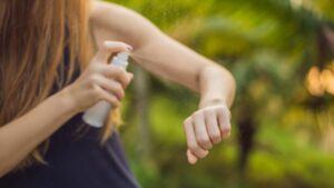 frau sprüht sich ein insektenschutzspray auf den nackten unterarm