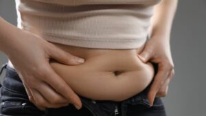 junge frau drückt beidseitig seitlich an ihren bauchfalten