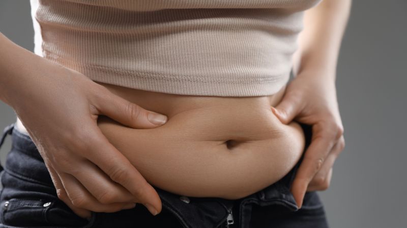junge frau drückt beidseitig seitlich an ihren bauchfalten